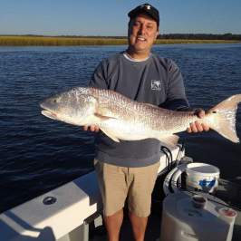 a man holding a fish in front of a body of water