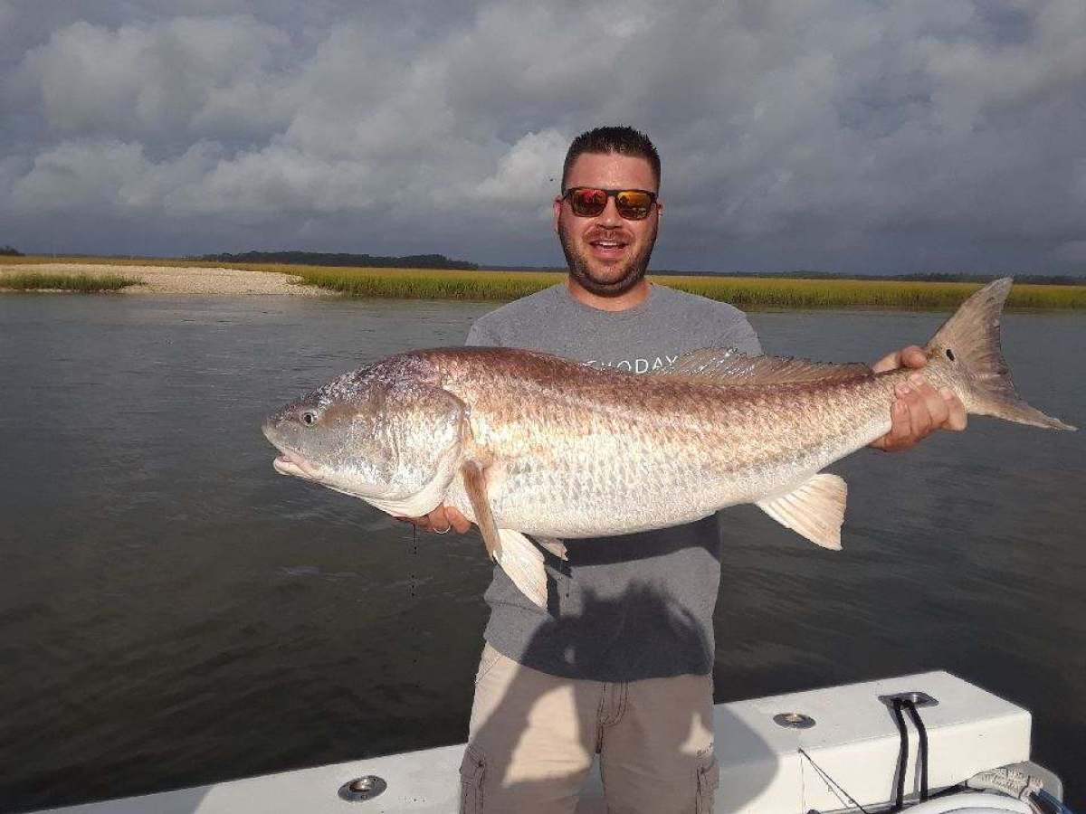 a man holding a fish in front of a body of water
