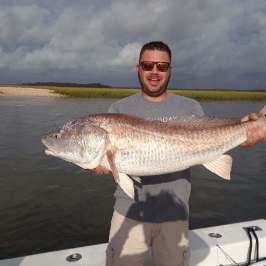 a man holding a fish in front of a body of water
